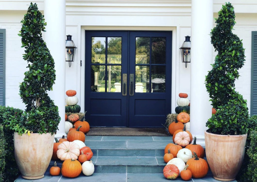 pumpkins for fall decorate a front porch with black door.