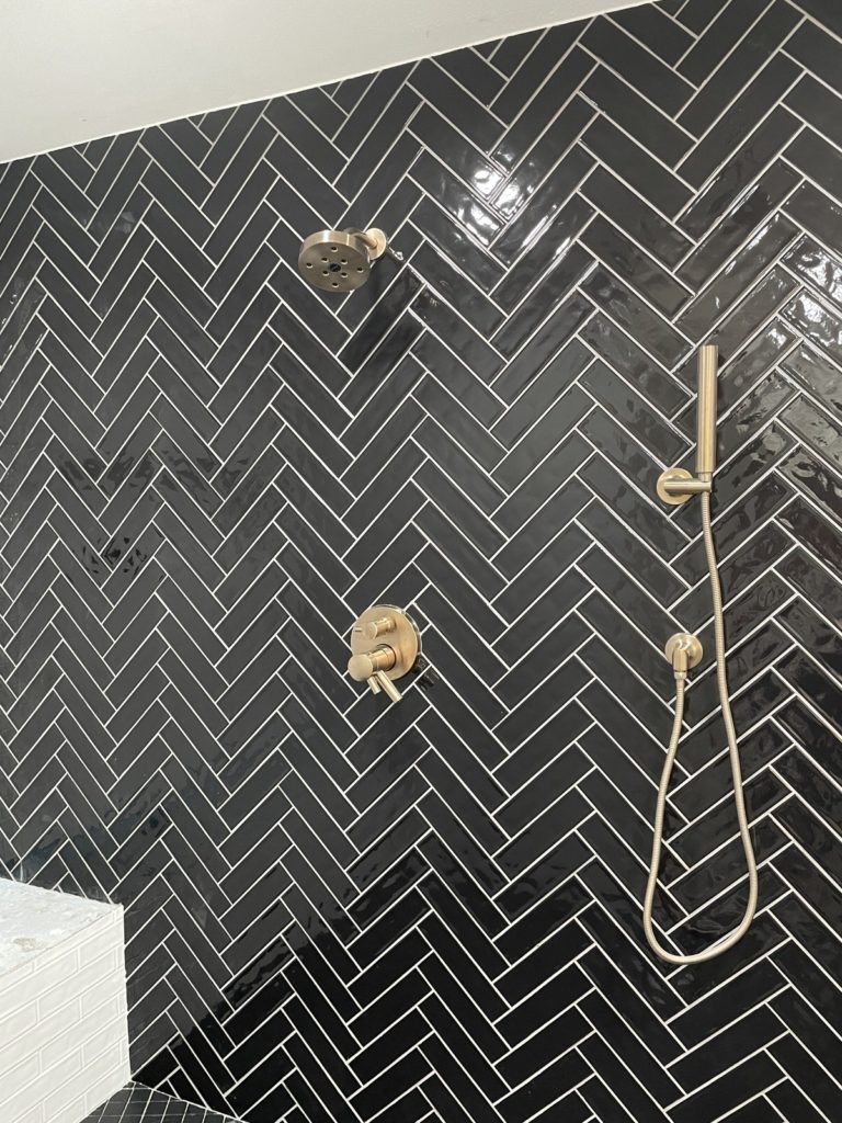 black herringbone tile shower with brass plumbing and white subway tile